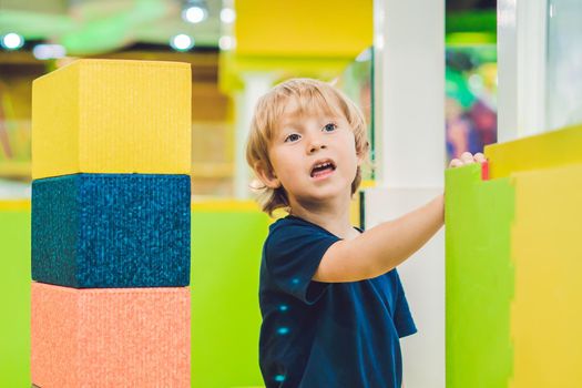 Happy boy playing indoors with big plastic construction blocks.