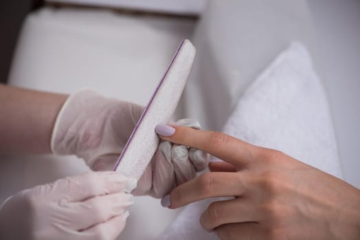 Woman hands receiving a manicure in beauty salon. Nail filing. Close up, selective focus.