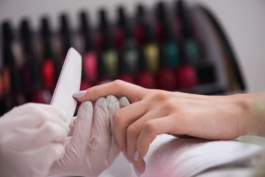 Woman hands receiving a manicure in beauty salon. Nail filing. Close up, selective focus.