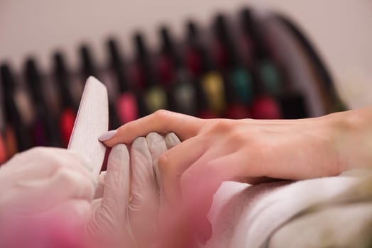 Woman hands receiving a manicure in beauty salon. Nail filing. Close up, selective focus.