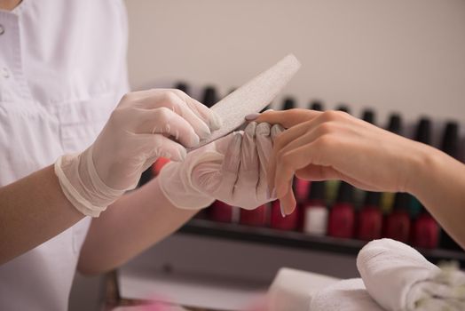 Woman hands receiving a manicure in beauty salon. Nail filing. Close up, selective focus.