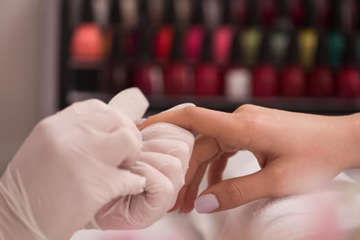 Woman hands receiving a manicure in beauty salon. Nail filing. Close up, selective focus.