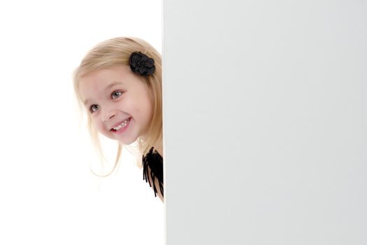 A nice little girl is looking because of an empty banner in which you can insert any text. The concept of a happy childhood, advertising, selling goods. Isolated on white background.