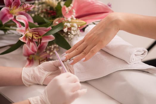 Woman hands receiving a manicure in beauty salon. Nail filing. Close up, selective focus.