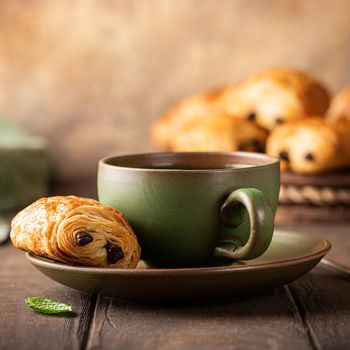 Green cup of tea with mini chocolate bun, puff pastry on old wooden table. Tasty tea break concept, copy space.