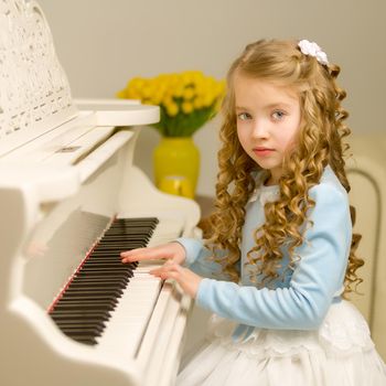 A nice little girl is playing on a big white piano. The concept of musical and aesthetic education of a child.