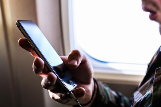 Closeup man using smartphone near window in airplane. Concept of modern technologe and low cost flights.