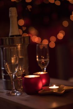 champagne and crystal glasses on a wooden table with candles and holiday lights in the background