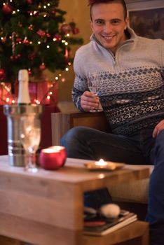 Portrait of a happy young man with a glass of champagne celebrating winter holidays at home beautifully decorated for Christmas