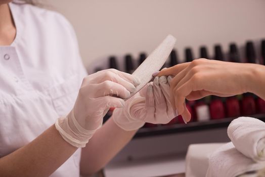 Woman hands receiving a manicure in beauty salon. Nail filing. Close up, selective focus.