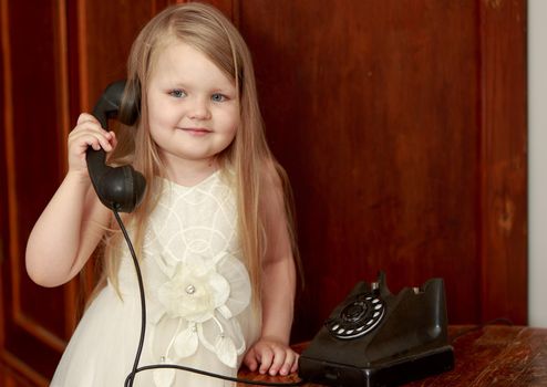 Cute little chubby girl with long, blonde hair below the shoulders, holds up the old phone