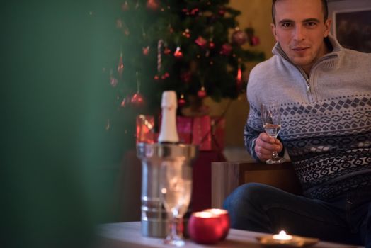 Portrait of a happy young man with a glass of champagne celebrating winter holidays at home beautifully decorated for Christmas