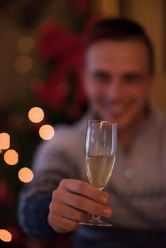 Portrait of a happy young man with a glass of champagne celebrating winter holidays at home beautifully decorated for Christmas