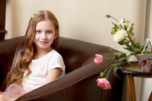 Happy little girl with a bouquet of flowers sitting on the couch. The concept of a holiday, a spring mood.