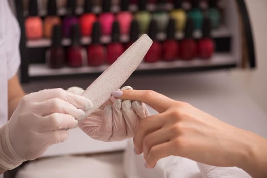 Woman hands receiving a manicure in beauty salon. Nail filing. Close up, selective focus.