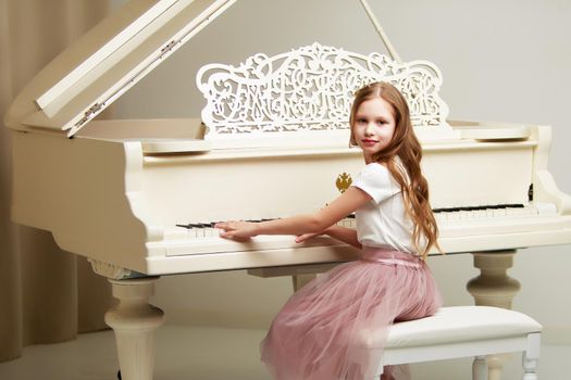 A nice little girl is playing on a big white piano. The concept of musical and aesthetic education of a child.