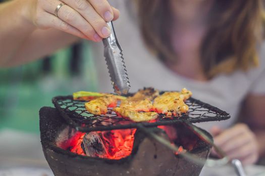 Girl frying meat on a small grill in a restaurant.