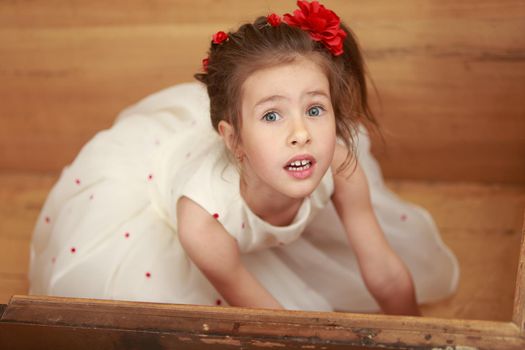 Cute little girl in a white dress hiding in the old chest, which smelled of mothballs. Girl looks out of it up