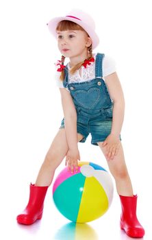 Beautiful little blonde girl with thin pigtails are braided in red ribbons, in denim overalls and red rubber boots playing with a ball - Isolated on white background
