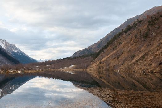 autumn landscape, lake in the mountains, water surface, fallen trees, coniferous forest and the first snow, mountains on the background