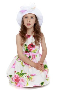 Gentle little girl in a white dress with roses and Panama. Girl sitting on the floor with his hands on his knees - Isolated on white background