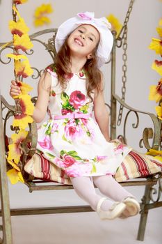 Gentle little girl in a white dress with roses and a white hat. Girl swinging on an old swing. Close-up