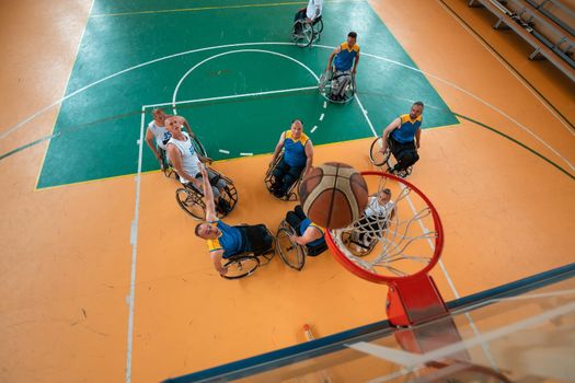 Disabled War or work veterans mixed race and age basketball teams in wheelchairs playing a training match in a sports gym hall. Handicapped people rehabilitation and inclusion concept. Top view.