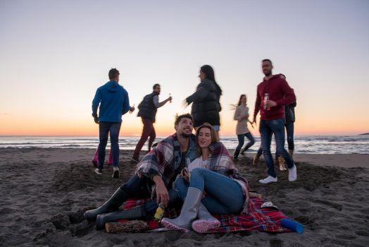 Young Couple enjoying with friends Around Campfire on The Beach At sunset drinking beer