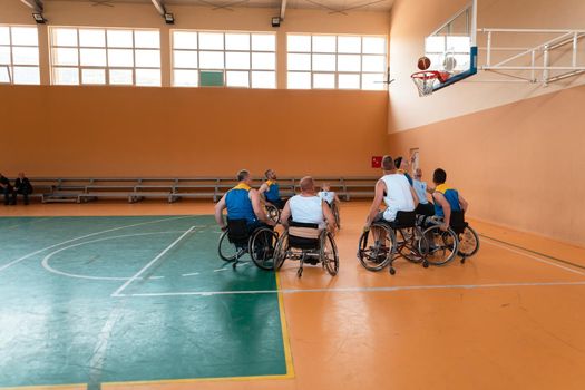 Disabled War or work veterans mixed race and age basketball teams in wheelchairs playing a training match in a sports gym hall. Handicapped people rehabilitation and inclusion concept.Hi quality photo