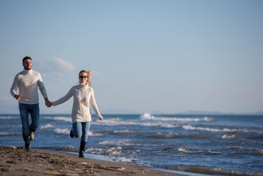 Young couple having fun walking and hugging on beach during autumn sunny day