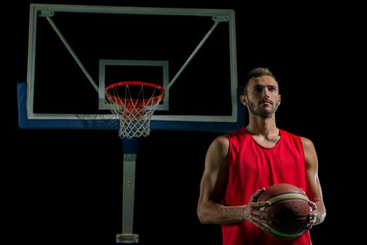 Basketball player portrait  on basketball court holding ball with black isolated background