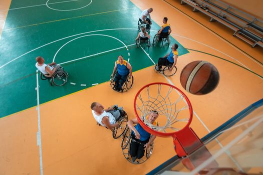 Disabled War or work veterans mixed race and age basketball teams in wheelchairs playing a training match in a sports gym hall. Handicapped people rehabilitation and inclusion concept. Top view.