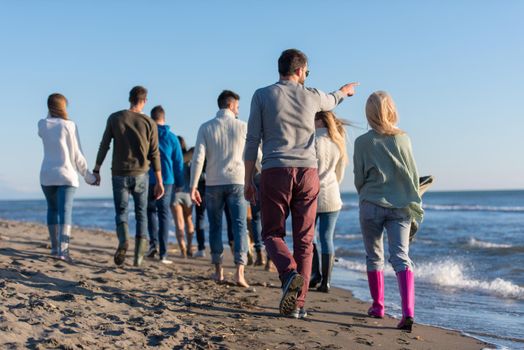 group of young friends spending day together running on the beach during autumn day