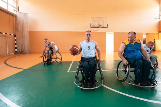 Disabled War or work veterans mixed race and age basketball teams in wheelchairs playing a training match in a sports gym hall. Handicapped people rehabilitation and inclusion concept.Hi quality photo