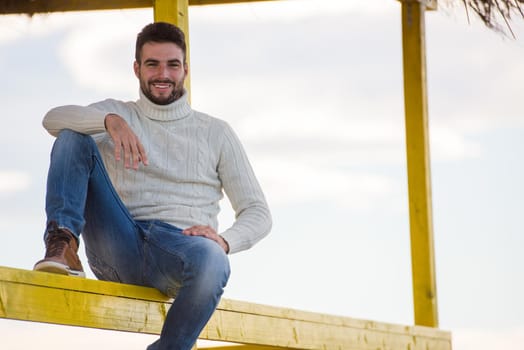 Young man on the beach. The guy enjoying the warm autumn day. Portrait of man near the water