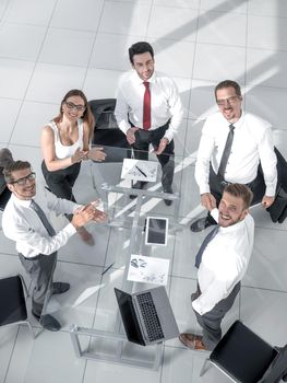 Smiling happy group of young business people working as a team seated around a table in the office looking up at the camera