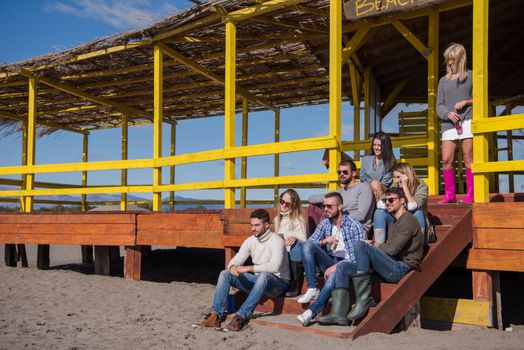 Happy Group Of Friends Hanging Out At Beach House having fun and drinking beer on autumn day