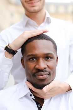 Caucasian man holding afro american guy head by hands.