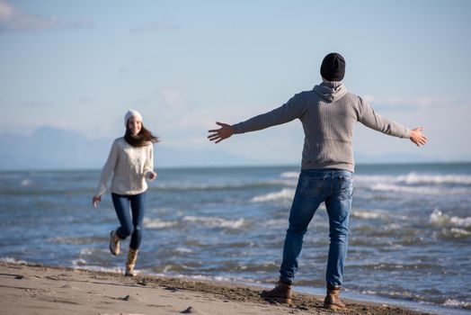 Young couple having fun walking and hugging on beach during autumn sunny day