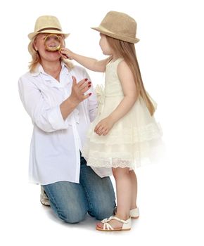 Cute little girl with long blond hair in white dress and hat . The girl looks at through a magnifying glass, the nose of his grandmother - Isolated on white background
