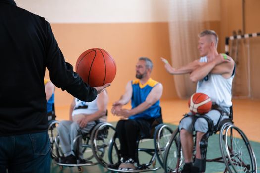 the selector of the basketball team with a disability stands in front of the players and shows them the stretching exercises before the start of training. Selective focus 