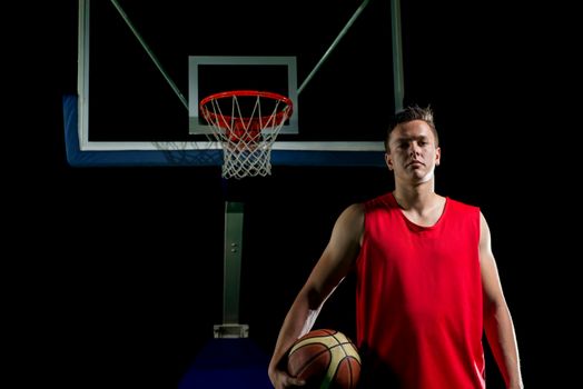 Basketball player portrait  on basketball court holding ball with black isolated background