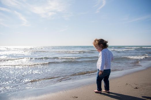 Adorable little girl having fun at beach during autumn day. Happy baby by the sea or ocean