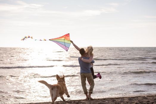 Young Couple having fun playing with a dog and Kite on the beach at autumn day