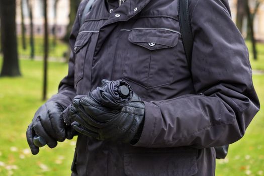 Close-up of man's hand in warm jacket and gloves holding closed umbrella after rain in park. Selective focus.
