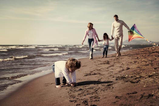 young family with kids resting and having fun with a kite at beach during autumn day filter