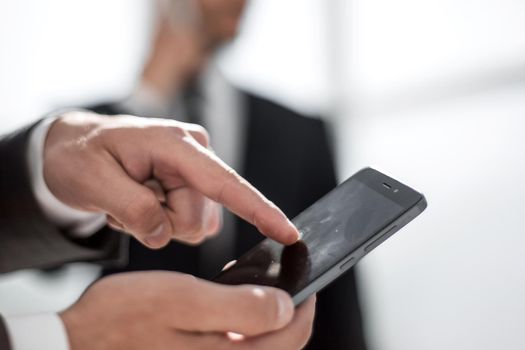 successful businessman pushes his finger on the phone screen. Finding information. Colleague on the background