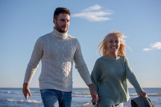 Young couple having fun walking and hugging on beach during autumn sunny day