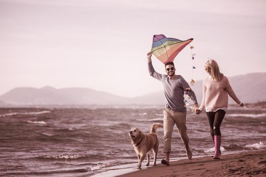 Young Couple having fun playing with a dog and Kite on the beach at autumn day filter