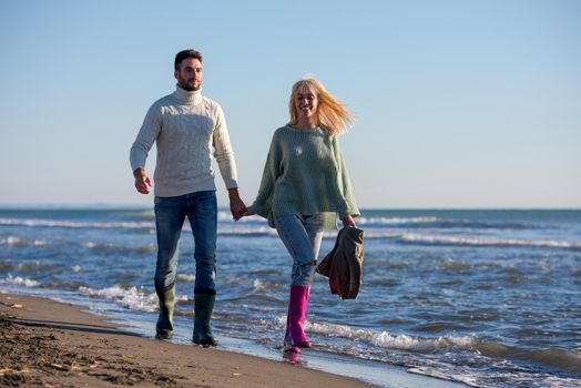 Young couple having fun walking and hugging on beach during autumn sunny day